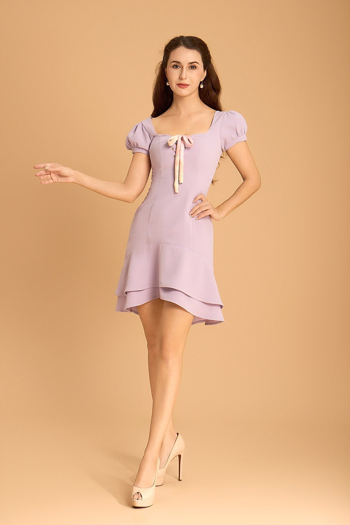 Model wearing a lilac Vanda Modes mini dress with puff sleeves, a double-tiered hem, and ribbon tie neckline - feminine, flattering, and newly released.